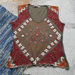 May include: A sleeveless, green tank top with a red, orange and white paisley print. The top has a v-neck and a scalloped hem.
