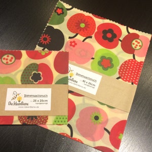 Könnte beinhalten: Zwei Blätter Bienenwachstuch mit einem Blumenmuster. Das größere Blatt ist 45 x 35 cm groß und das kleinere 25 x 25 cm. Beide Blätter sind handgefertigt und haben ein Bienenlogo mit dem Text "Die IdeenBiene" und einer Website-Adresse.