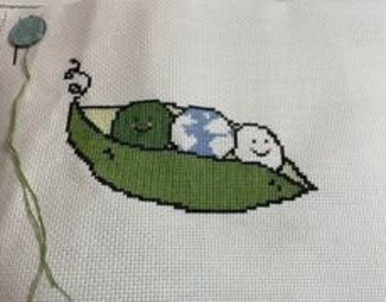 May include: Cross-stitch embroidery of three green peas in a pea pod. The peas have smiling faces and one has a blue and white pattern.