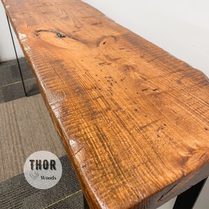 May include: A rustic wooden console table with a live edge top and black metal legs. The table has a natural wood finish and is made from reclaimed wood. The table is approximately 48 inches long and 16 inches wide.