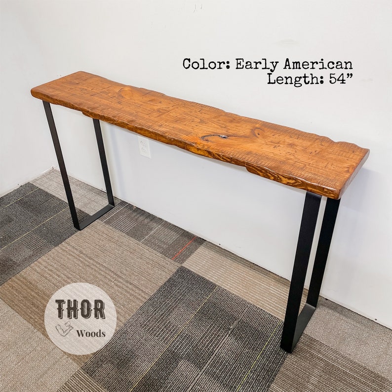 May include: A long, narrow console table with a live edge, natural wood top in an Early American stain. The table has a black metal frame and is 54 inches long.