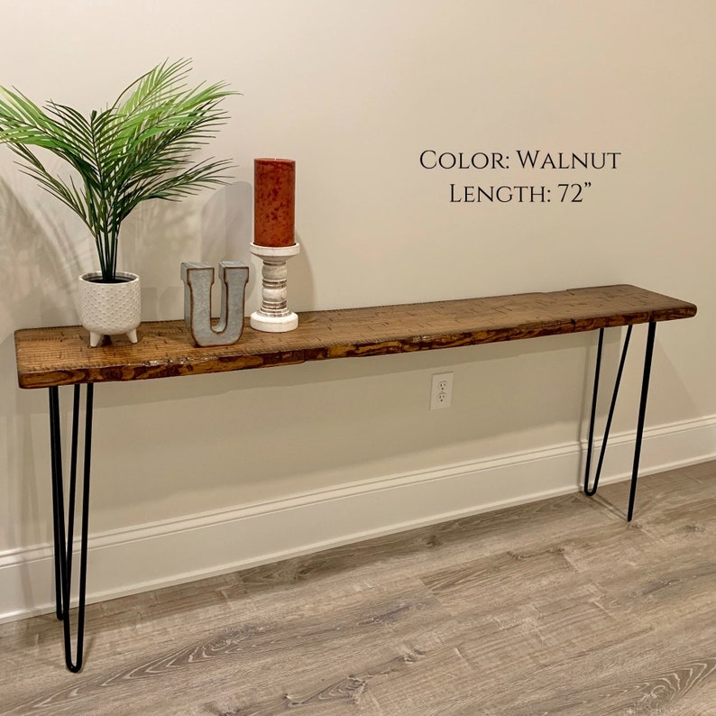 Puede incluir: Una mesa consola de nogal de 183 cm de largo con una tapa de borde vivo y patas de horquilla negras. La mesa est&aacute; decorada con una planta en maceta, una vela y una letra decorativa U.
