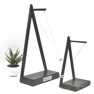 May include: Two black wooden pendulum stands with a silver ball and ring attached to a string. The stands have a triangular base and a horizontal bar at the top. The larger stand has a silver plaque with the text "The Perpetual Pendulum" on the base.