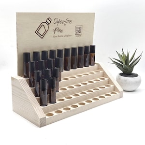 May include: A wooden display stand with multiple levels, holding numerous small, brown glass bottles with black caps. The stand has the text "Superfine Pine" and a bottle graphic. A small plant in a white pot is to the right.