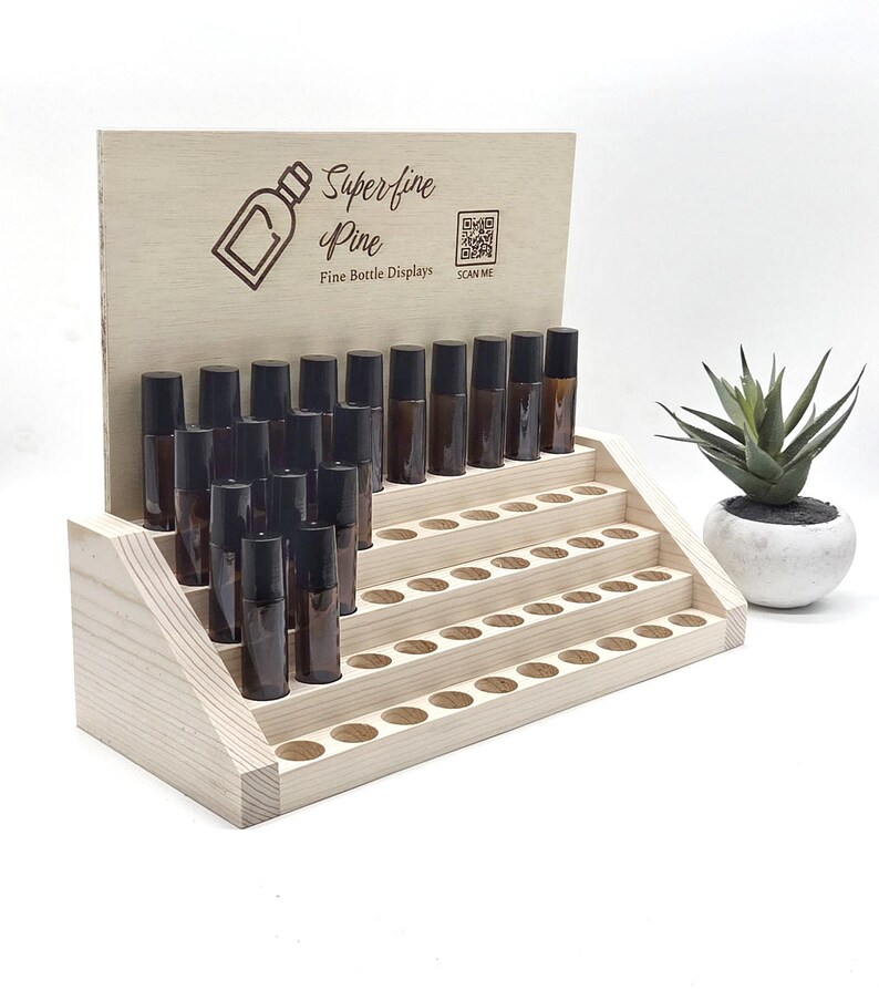 May include: A wooden display stand with multiple levels, holding numerous small, brown glass bottles with black caps. The stand has the text "Superfine Pine" and a bottle graphic. A small plant in a white pot is to the right.
