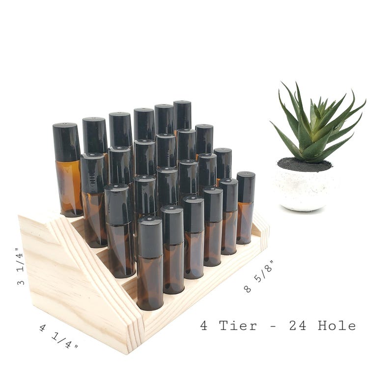 May include: A wooden essential oil display stand with 24 holes, arranged in four tiers. The stand holds numerous amber glass roller bottles with black caps. A small succulent plant in a white pot is in the background. The stand measures 8 5/8" long, 4 1/4" wide, and 3 1/4" high.