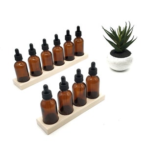 May include: A set of ten amber glass bottles with black droppers, organized in two rows on a wooden stand. The bottles are arranged in a staggered pattern, with the droppers facing outward. The stand is made of light-colored wood and has a natural finish.