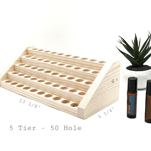 May include: A natural wood essential oil display stand with five tiers and 50 holes. The stand is 13 1/8 inches long, 5 1/4 inches wide, and 4 inches tall. Two essential oil bottles and a small potted plant are next to the stand.