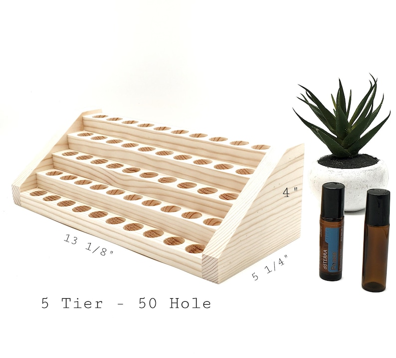 May include: A natural wood essential oil display stand with five tiers and 50 holes. The stand is 13 1/8 inches long, 5 1/4 inches wide, and 4 inches tall. Two essential oil bottles and a small potted plant are next to the stand.