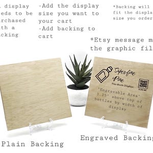 May include: Two wooden display backings, one plain and one engraved with "Superfine Pine" and a bottle graphic. The engraved backing includes text about the engravable area. Both are displayed on clear stands, with a potted succulent in the background.
