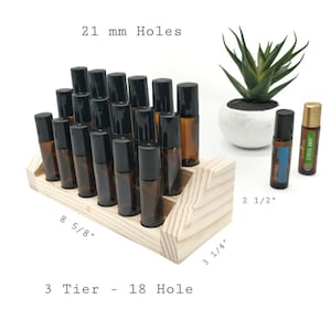 May include: A three-tiered, 18-hole wooden essential oil display stand. The stand holds several amber glass roller bottles with black caps. The stand measures 8 5/8" long, 3 1/4" wide, and 2 1/2" tall. The holes are 21 mm.