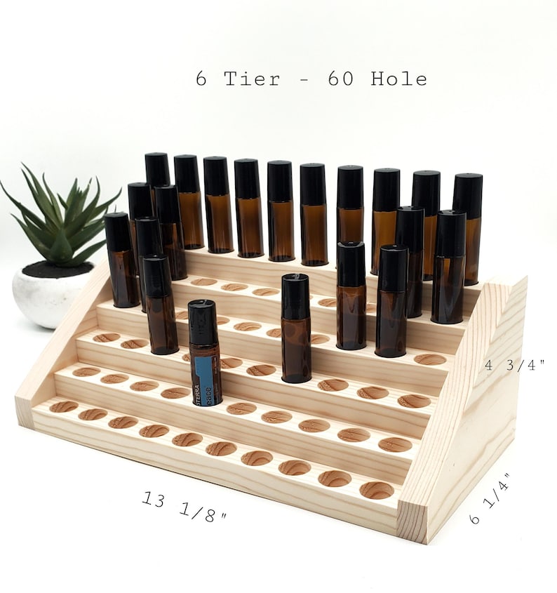 May include: A six-tier wooden essential oil display rack with 60 holes. The rack is 13 1/8 inches long, 6 1/4 inches high, and 4 3/4 inches deep. The rack holds several amber glass roller bottles with black caps. The text "6 Tier - 60 Hole" is visible.