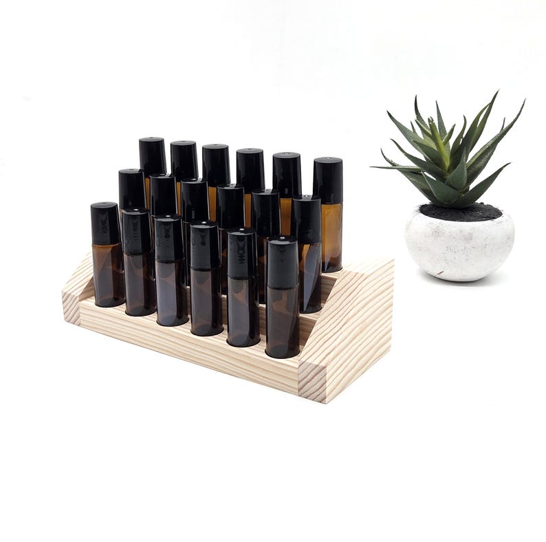 May include: A wooden display stand holds multiple amber glass roll-on bottles with black caps. A small potted succulent plant sits to the right. The bottles are arranged in rows, showcasing a product for essential oils or perfumes.