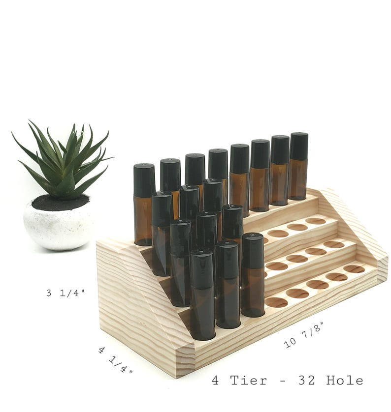 May include: A wooden, 4-tier essential oil roller bottle display with 32 holes. The display holds several amber glass roller bottles with black caps. A small succulent plant in a white pot is to the left of the display.