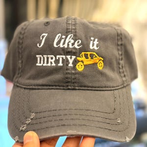 May include: Gray baseball cap with the embroidered text "I like it DIRTY" and a yellow off-road vehicle. The cap has a distressed look with frayed edges.