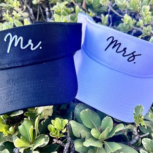 May include: Two visors, one black and one light blue, with the words "Mr." and "Mrs." embroidered in white and black thread, respectively.