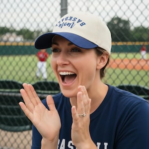 May include: A baseball cap with a cream-colored crown and a navy blue brim. The front of the cap features the text "baseball mom" embroidered in navy blue thread, with the word "baseball" arched over the word "mom" in a script font.