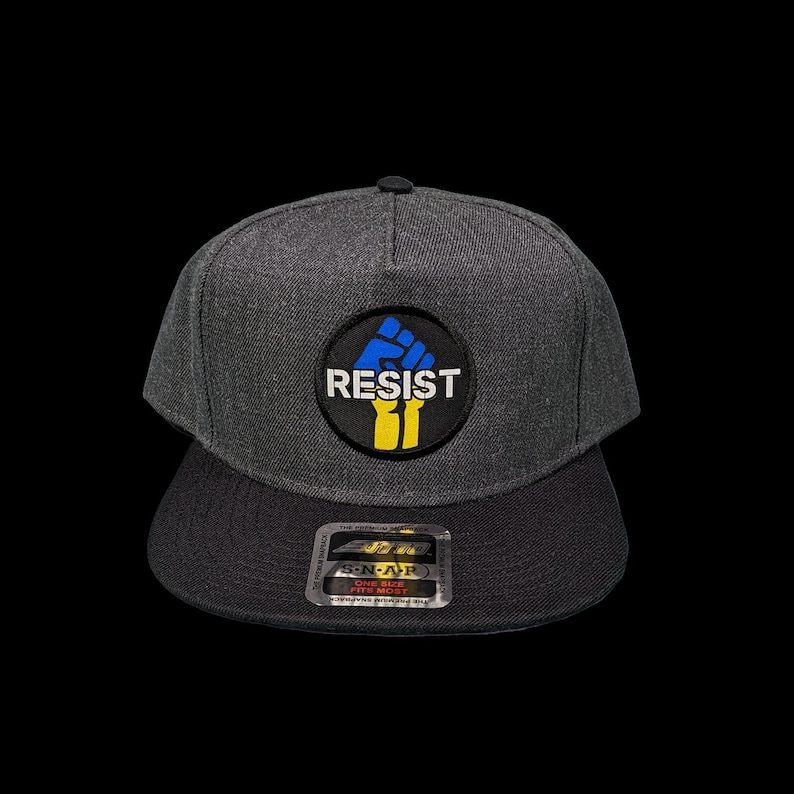 May include: A gray and black baseball cap with a black and yellow fist graphic and the word "RESIST" in white letters.