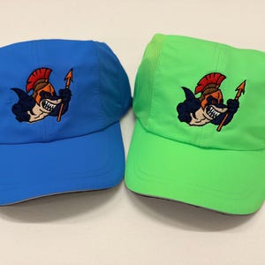 May include: Two athletic caps, one blue and one neon green, featuring an embroidered graphic of a shark wearing a red-crested helmet and holding a spear. Both hats have mesh side panels and a curved brim, showcasing a consistent design.