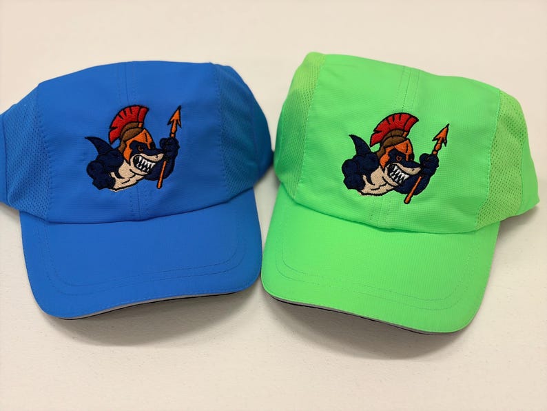 May include: Two athletic caps, one blue and one neon green, featuring an embroidered graphic of a shark wearing a red-crested helmet and holding a spear. Both hats have mesh side panels and a curved brim, showcasing a consistent design.