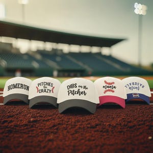 May include: Five baseball caps with white crowns and colored brims. The caps feature black text reading HOMERUN, PITCHES Be CRAZY, DIBS on the Pitcher, mama with red baseball stitching, and blue text reading BASEBALL mom with a small rectangular patch.