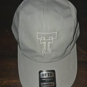 May include: A light gray baseball cap featuring a white embroidered double T logo on the front panel. The cap includes side mesh ventilation panels and a black sticker on the brim with the text OTTO PERFORMANCE OSFM RUNNING.