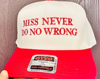 May include: A white and red baseball cap with the embroidered text "MISS NEVER DO NO WRONG". The cap has a red brim and a white crown. The cap has a "OTTO" label.
