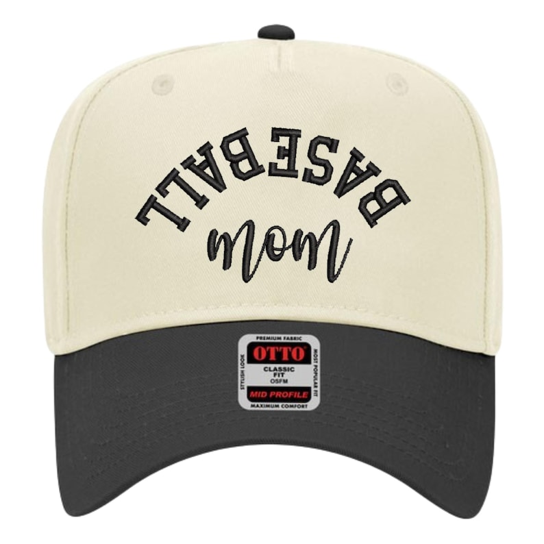May include: A two-tone baseball cap with a cream-colored crown and a black brim. The front features black embroidered text that reads BASEBALL in an arched block font above the word mom in a cursive script. A square sticker is on the brim.