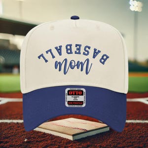 May include: A cream-colored baseball cap with a dark blue brim and dark blue embroidered text that reads BASEBALL mom. The cap features a central button on top and a rectangular sticker on the brim with the text OTTO CLASSIC FIT OSFM.