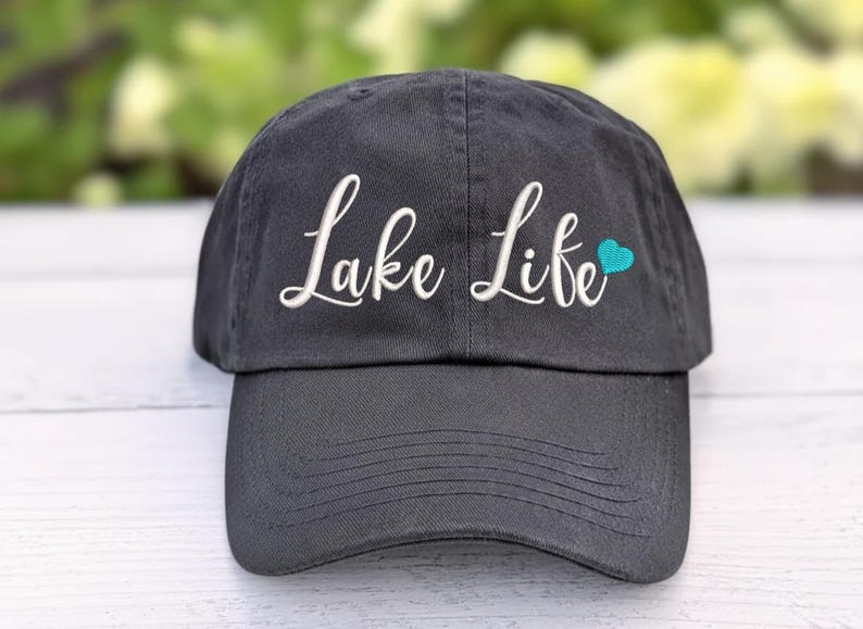 以下が含まれることがあります： 白い筆記体で「Lake Life」と刺繍された、小さなターコイズのハートが付いた濃い灰色の野球帽。 つばがカーブしており、柔らかい生地で作られています。