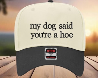 May include: A cream-colored baseball cap with a black brim and a black button on top. The cap features the text "my dog said you're a hoe" in black letters. A small tag is visible on the front.
