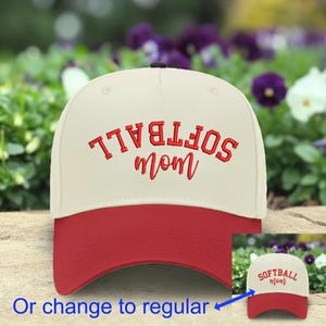 May include: A cream-colored baseball cap with a red brim and red embroidered text on the front. The text reads SOFTBALL in a block font and mom in a cursive script. The word SOFTBALL is printed upside down in the main image, with a small inset.