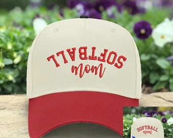 May include: A cream-colored baseball cap with a red brim and red embroidered text on the front. The text reads SOFTBALL in a block font and mom in a cursive script. The word SOFTBALL is printed upside down in the main image, with a small inset.