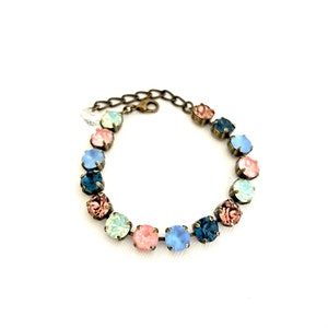 May include: A delicate bracelet featuring a series of colorful, round gemstones in shades of pink, blue, and green. The stones are set in a bronze-toned metal, connected by a matching chain. The bracelet is designed to be worn around the wrist.