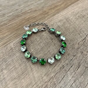 May include: A silver bracelet with a graduated ombre of green crystals. The bracelet is made of metal and has a chain link closure.