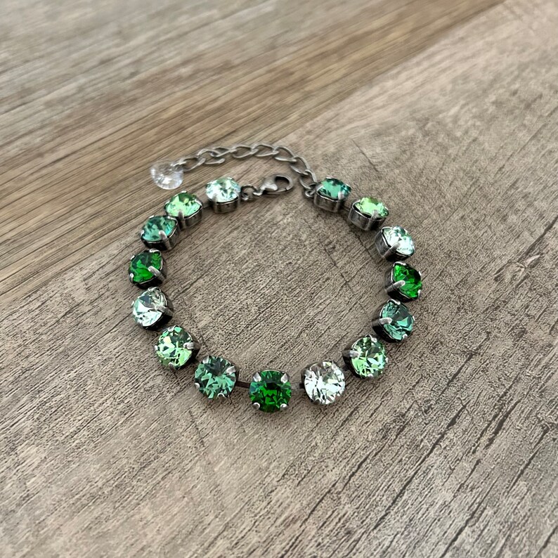 May include: A silver bracelet with a graduated ombre of green crystals. The bracelet is made of metal and has a chain link closure.