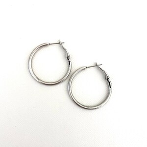 May include: A pair of silver hoop earrings. The earrings are simple and elegant, with a smooth, slightly textured finish.