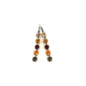 May include: A pair of dangle earrings with a gradient of square-cut crystals in shades of beige, orange, and brown. The earrings have a silver-tone metal hook closure. The crystals are arranged in a vertical line, creating a cascading effect.