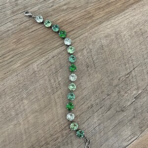 May include: A silver bracelet with a gradient of green crystal beads. The beads are round and have a faceted finish.