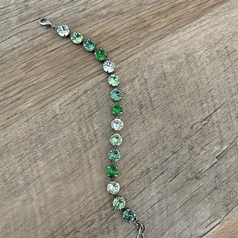 May include: A silver bracelet with a gradient of green crystal beads. The beads are round and have a faceted finish.