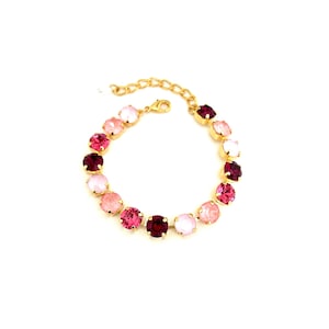 May include: A gold-toned bracelet featuring a series of round, colorful gemstones. The gemstones are in shades of pink, ranging from light blush to deep magenta, and are set in a gold metal chain. The bracelet is displayed on a white background.