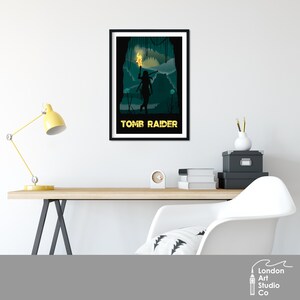 Puede incluir: Un p&oacute;ster en blanco y negro con una silueta de una mujer sosteniendo una antorcha en un entorno de jungla. El texto "Tomb Raider" est&aacute; en la parte inferior del p&oacute;ster.