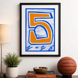 Op de afbeelding: Een ingelijste muurkunstprint met een groot, vet oranje cijfer 5 met een blauwe omlijning op een getextureerde witte achtergrond. Onder het cijfer staat de tekst 2026 in een blauwe, handgeschreven stijl. De print zit in een zwarte lijst.