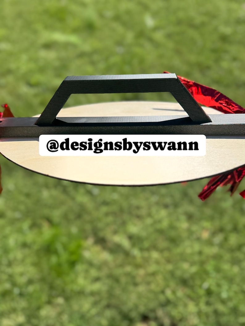 May include: A wooden serving tray with a black handle. The tray is round with a light wood finish. The text "@designsbyswann" is printed on the tray. Red decorative accents are visible.
