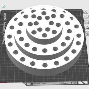 May include: A white, tiered, cylindrical object with a series of circular holes arranged in concentric patterns on its top surface. The object is positioned on a dark gray grid-patterned base labeled Bambu Textured PEI Plate.