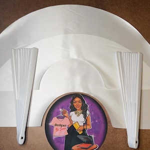 May include: Three white satin fabric fan shapes, two white paper folding fans, and a round sticker with a woman wearing a white shirt with the text "Designers By Jasmine" on it.