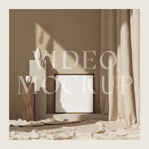 May include: A white square video screen mockup in a brown frame, sitting on a white platform in a beige room with a beige curtain and a dried plant in a white vase on a wooden pedestal.