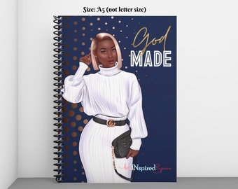 May include: A spiral-bound notebook with a cover featuring an illustration of a woman in a white turtleneck sweater and a black belt. The words "God Made" are written in gold script on a navy blue background with gold dots. The notebook is A5 size.