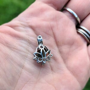May include: Silver lotus flower charm pendant with a delicate openwork design. The pendant is shown in the palm of a hand.