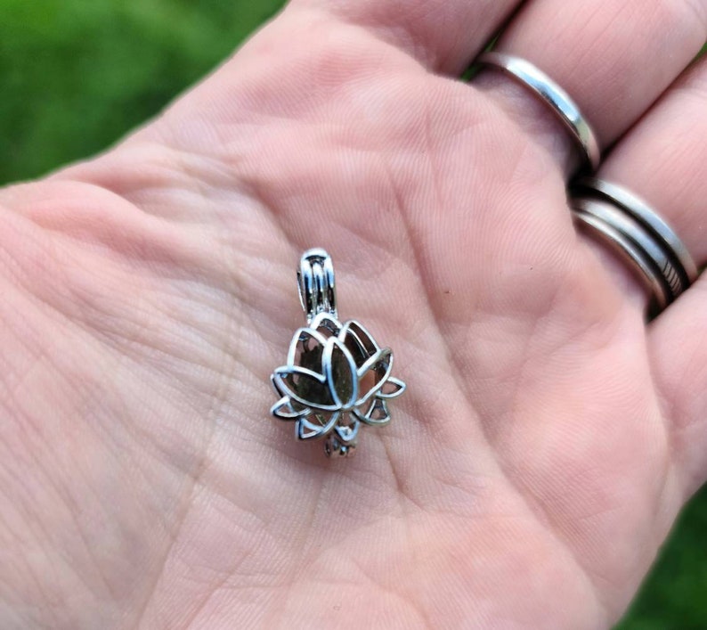 May include: Silver lotus flower charm pendant with a delicate openwork design. The pendant is shown in the palm of a hand.